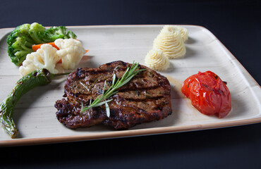 Steak with boiled vegetables, mashed potatoes and tomatoes close up