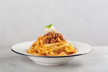 Egg pasta tagliatelle with bolognese sauce made from meat and tomato sauce. Traditional italian dish from Bologna. With hard cheese. Minimalism. Light grey background. 