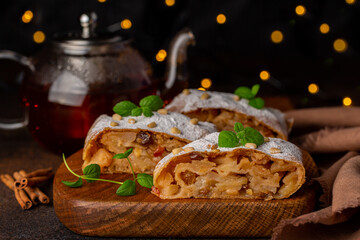 Apple strudel with hot tea. Christmas lights on dark background.