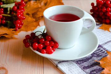 Obraz na płótnie Canvas Autumn healthy beverages concept. Cup of tea with autumn berries viburnum and fall leaves. Drink with vitamin c