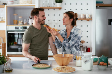 Young couple making pancakes at home. Loving couple having fun while cooking.