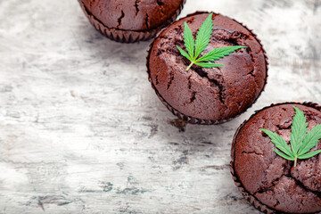 Chocolate cupcake muffins with cannabis leaves weed cbd. Medical marijuana hemp drugs in food dessert. Cooking baking weed muffins with marijuana on gray concrete background. Copy space Closeup
