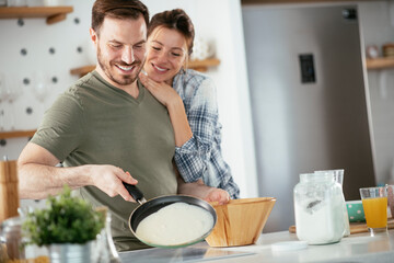 Young couple making pancakes at home. Loving couple having fun while cooking.