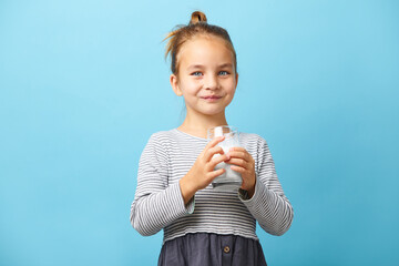 portrait of smiling child girl holding glass of milk on blue isolated.