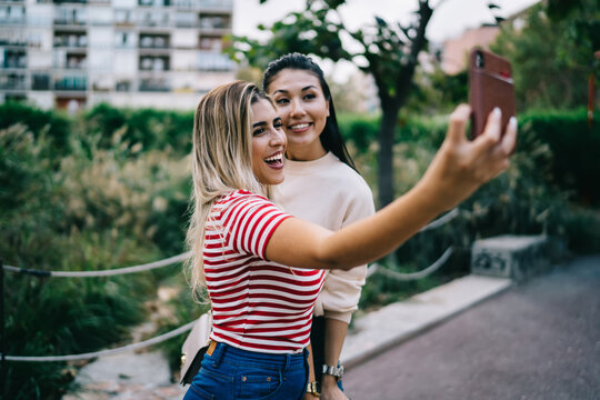 Happy multiracial female bloggers millennial influencers making selfie on smartphone camera, cheerful woman best friends spending time together outdoors having fun making pictures on mobile phone