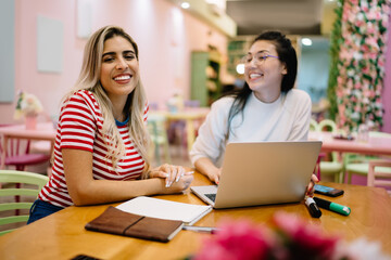 Portrait of cheerful Hispanic hipster girl laughing at camera during collaborative meeting with blurred freelance colleague, happy female students 20 years old enjoying e learning togetherness