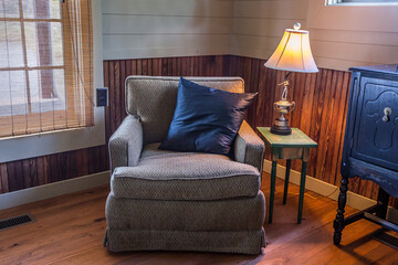 a gray comfortable armchair with a navy blue pillow, a side table and a lamp in a rustic hunting...