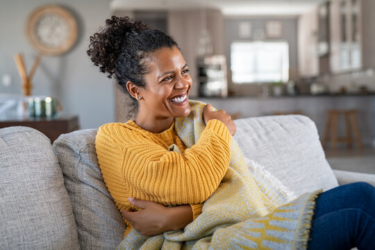 Joyful african woman with blanket on couch laughing