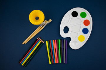 
Items for drawing on a blue background. Markers, pencils, color palette with brushes. View from above.