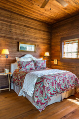 Rustic cabin bedroom with a large bed, quilt and wood-paneled walls and ceiling