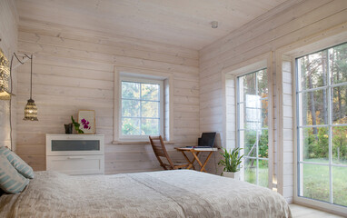 White bedroom with simple decor items in a stylish wooden house. Workplace in the bedroom, a table and a computer