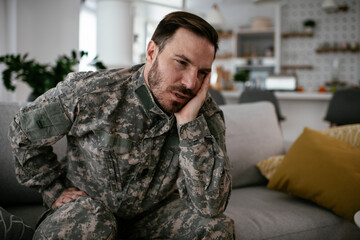 Fototapeta premium Depressed soldier sitting on sofa in living room. Young marine having PTSD..
