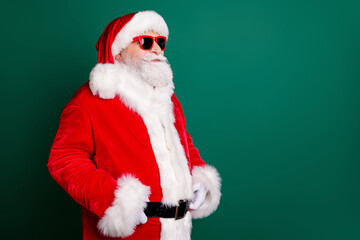 Photo of pensioner grandpa grey beard self-assured hands belt look empty space watch children make snowman wear red santa costume coat gloves sunglass headwear isolated green color background