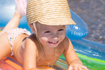 Little girl in a wicker cap floats on an air mattress in the sea