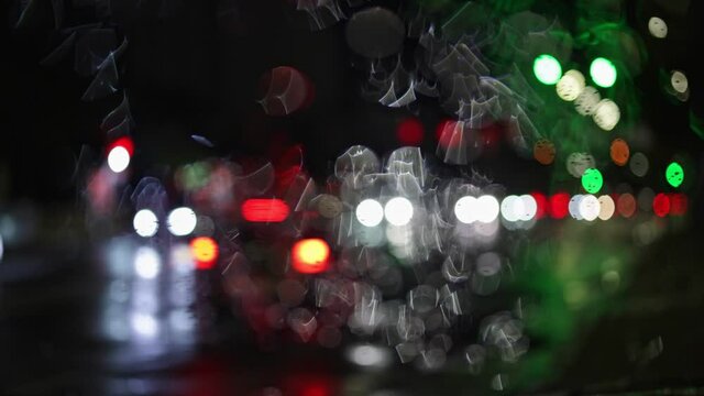 Night city traffic through the wet car window. Abstract bokeh lights of passing cars. Rainy autumn weather. Slow motion 4K