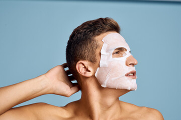 Nude man with white nourishing mask on face on blue background cropped view