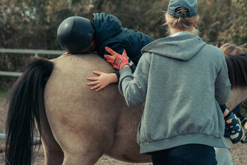 A little boy in turquoise overalls stroking an Icelandic pony horse with a funny forelock. The kid...
