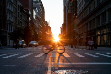 Woman riding a bike down the street in Midtown Manhattan, New York City with sunlight shining in the background
