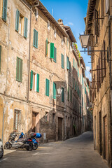 A narrow medieval street with brick houses, lanterns and motorcycles in Siena, Italy