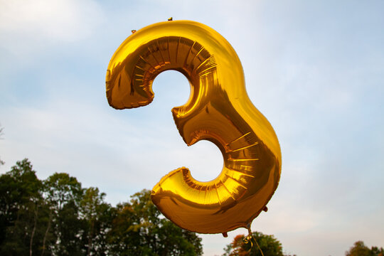 A balloon of gold color in the form of a number three in the park - Powered by Adobe