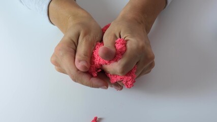 Hands crushing and crumpling pink plasticine with small balls inside, anti stress and relaxing game, close up