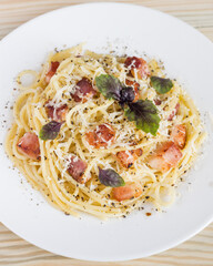 Pasta Carbonara. Spaghetti with bacon, parmesan cheese and basil on white plate on light wooden background. Italian food concept. Top view, close-up.