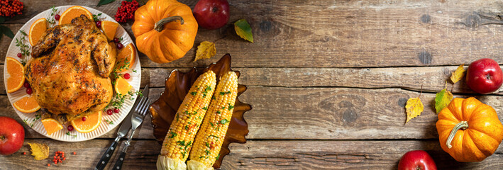 Autumn festive Thanksgiving background. Baked chicken or turkey, festive food for Thanksgiving dinner on wooden table. Table settings for Thanksgiving. Long format with copy space