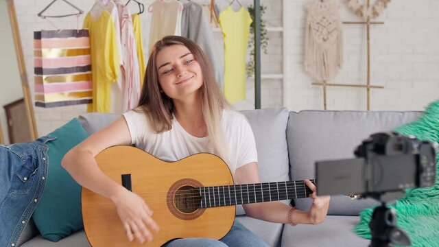 Attractive Teenager Girl Vlogging During Playing on a Guitar.Young Girl Conduct Remote Teaching to Play on a Guitar During Blogging.