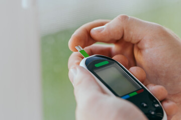 diabetes, healthcare - close up of a man with a glucometer and a test strip checking blood sugar at home
