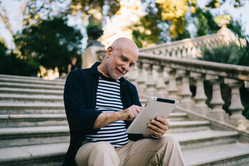 Obraz premium Happy senior male surfing tablet on stairs in park