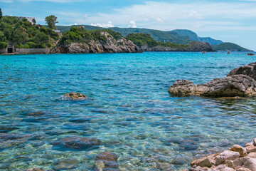 Beautiful landscape - sea lagoon with turquoise calm water, stones and rocks on the beach, blue sky. Corfu Island, Greece.