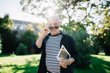 Fototapeta premium Serious stylish 50 years old male with sunglasses and tablet in city park