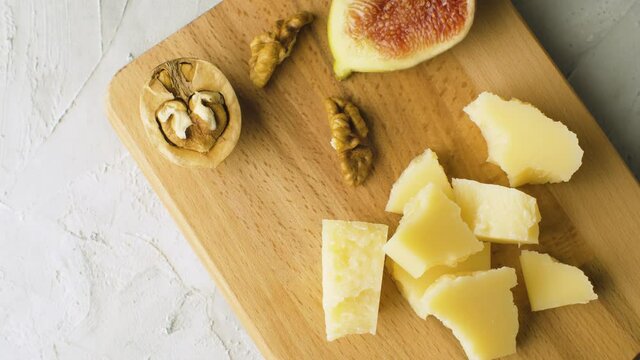 Macro shot cheese, walnuts and half fig on a wooden cutting board. Healthy fresh food concept. Close up, camera slowly moving on the slider, top view, dolly shot