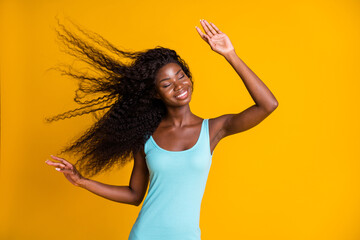 Photo portrait of african american woman dancing in gentle wind one raised hand wearing blue tank-top isolated on vivid yellow colored background