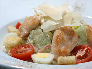 Caesar salad with chicken, egg, tomatoes and parmesan on a white plate