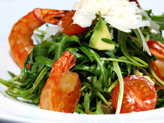 Arugula salad with shrimp, avocado, tomatoes and parmesan on a white plate