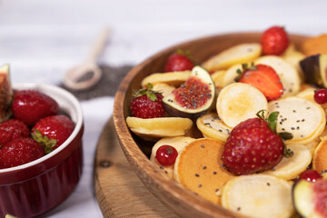 Small pancakes with strawberry, currant and slieces of figs on white table. Top view of treandy breakfast.