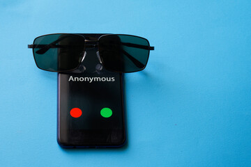 A smartphone with an anonymous call lies on a blue surface next to sunglasses. The problem of...
