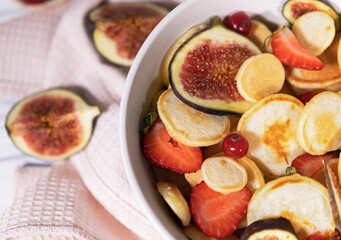 Small pancakes with strawberry, currant and slieces of figs on white table. Top view of treandy breakfast.