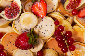 Small pancakes with strawberry, currant and slieces of figs. Top view of treandy breakfast.