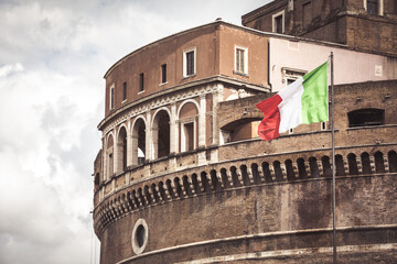 Detail of Castel Sant'Angelo Mausoleum of Hadrian in Rome with Italian flag. Ancient and historic castle monument in Italy. Towering cylindrical building.