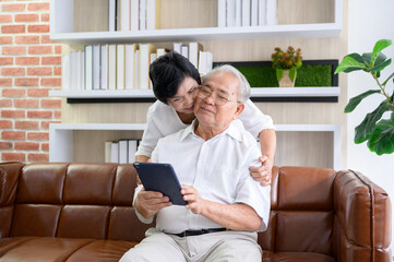 A happy senior Asian couple is using tablet and talking with family on webcam at home, retirement concept.