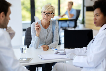 Fototapeta premium Mature woman talking to doctors during medical appointment at clinic.