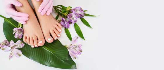 Beautiful perfect female skin legs feet top view with tropical flowers and green palm leaf. Nail...