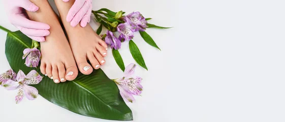 Fototapeten Beautiful perfect female skin legs feet top view with tropical flowers and green palm leaf. Nail polish, care and clean, spa pedicure treatment in white. Concept on background isolated. Copy space © Алина Троева