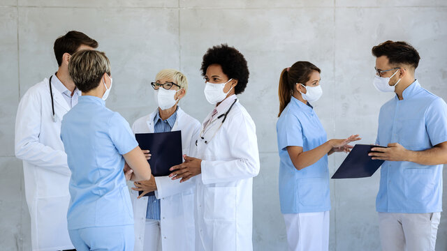 Group Of Healthcare Workers With Protective Face Masks Talking At Hospital Hallway.