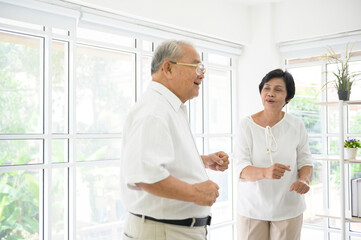 Obraz premium joyful senior asian retired couple is dancing and enjoying the music in the living room at home, health concept