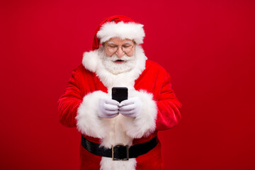 Portrait of his he nice attractive handsome cheerful cheery focused Santa using gadget 5g fast speed blog blogger post comment media isolated over bright vivid shine vibrant red color background