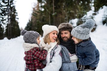 Father and mother with two small children in winter nature, standing in the snow.