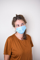 young woman in a medical mask and home clothes looks at the camera isolated on a colored...